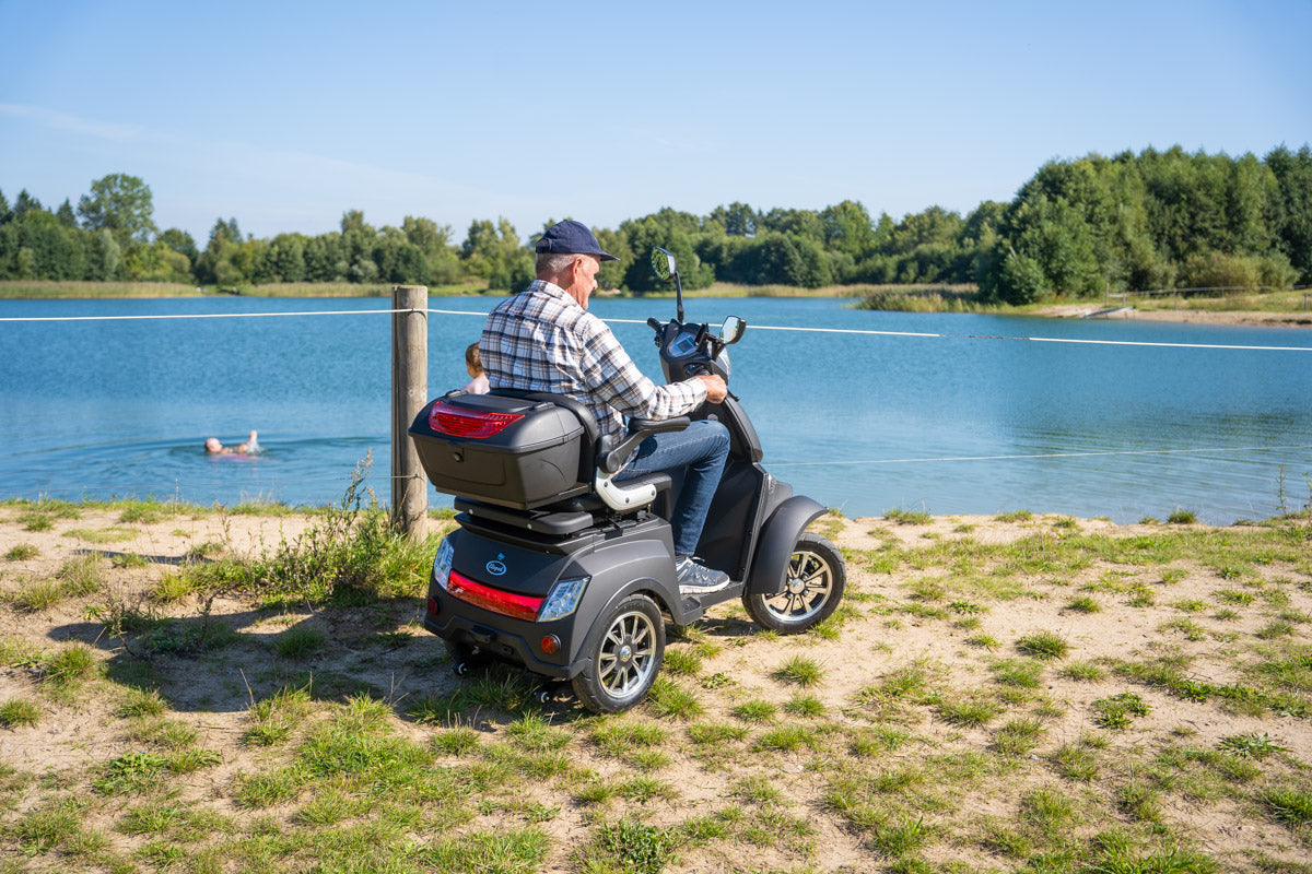 Äldre man sitter på promenadscooter med fyra hjul vid en sjö